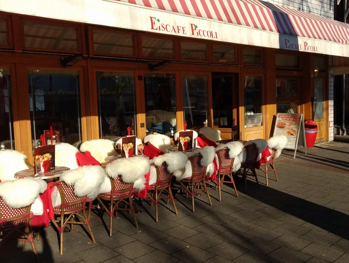 28616543_1876379535705811_6119886081932960166_o.jpg Das Bild zeigt den Außenbereich des Eiscafes PiccolIis. Man erkennt viele gemütliche Sitzgelegenheiten.