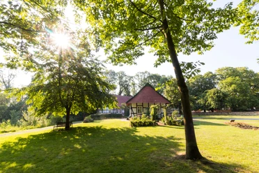 Ein malerisches Fachwerkhaus in einem sonnigen Park, umgeben von Bäumen und einer grünen Wiese.