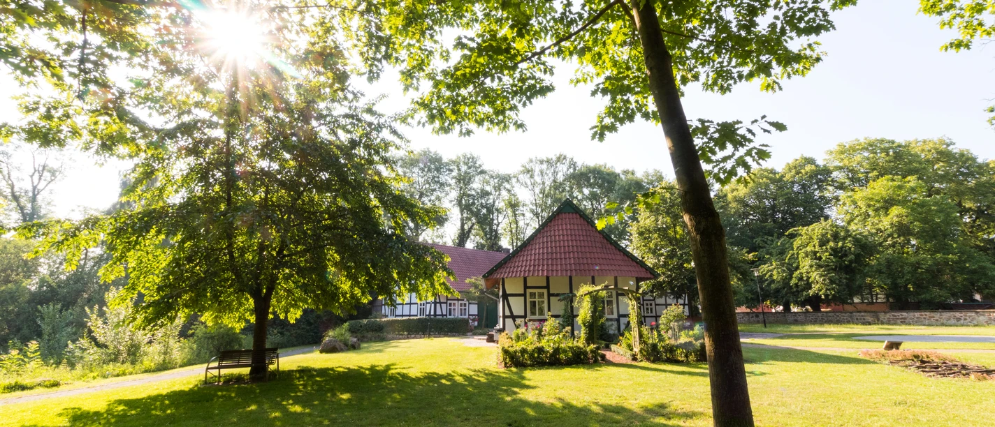 Ein malerisches Fachwerkhaus in einem sonnigen Park, umgeben von Bäumen und einer grünen Wiese.