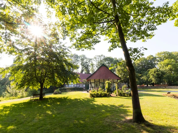 200613-FotoChristianSchwier-_Rothenuffeln.jpg Ein malerisches Fachwerkhaus in einem sonnigen Park, umgeben von Bäumen und einer grünen Wiese.