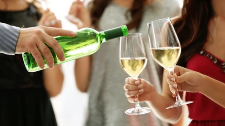 Weinfest Greetsiel Eine Person schenkt weißen Wein in zwei Gläser, Menschen halten sie bei einem Fest im Freien.