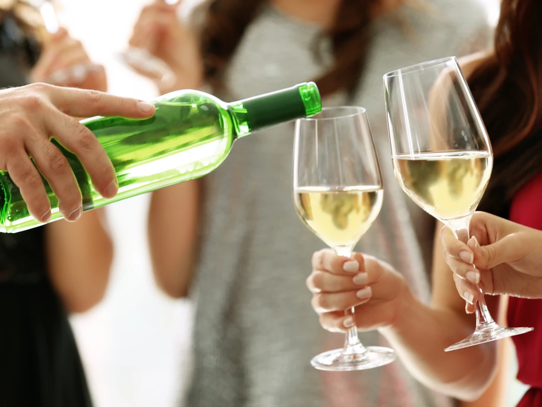 Weinfest Greetsiel Eine Person schenkt weißen Wein in zwei Gläser, Menschen halten sie bei einem Fest im Freien.