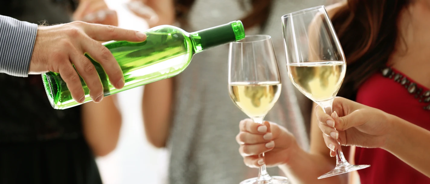 Weinfest Greetsiel Eine Person schenkt weißen Wein in zwei Gläser, Menschen halten sie bei einem Fest im Freien.