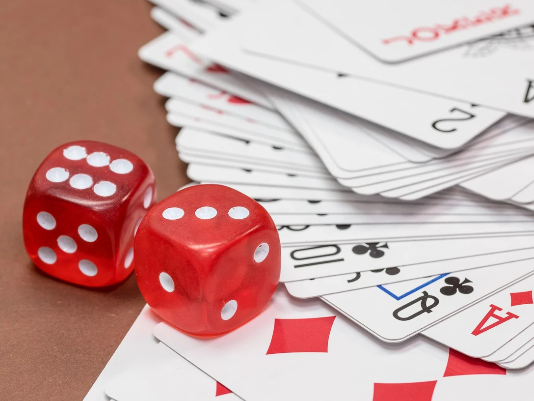 wuerfel-skatblatt_Michael Schwarzenberger auf Pixabay.jpg Zwei rote Würfel liegen auf einem zerstreuten Skatblatt mit gut sichtbaren Spielkartenzeichen.