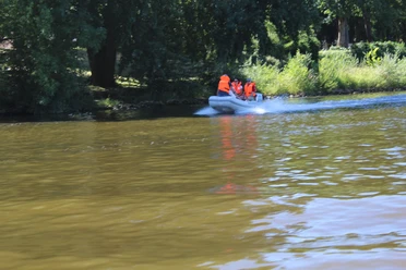 Gruppe in einem Motorboot mit orangenen Westen fährt auf einem Fluss, umgeben von grünen Bäumen.