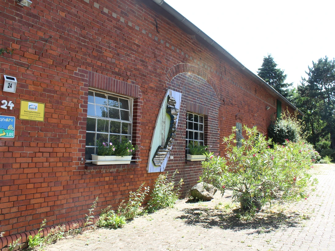 Reelingehof-Pension, Petershagen Ziegelrote Fassade des Reelingehofes mit blühenden Blumenkästen und einer kunstvollen Skulptur.