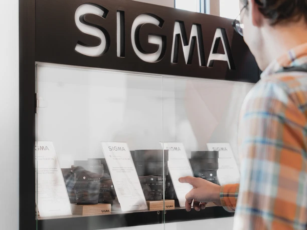 Een klant bekijkt lenzen in de display van de SIGMA verhuurwinkel in Bad Schandau bij daglicht.