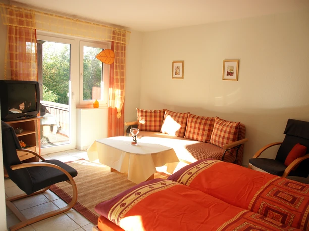 20.jpg Helles Wohnzimmer mit Sofa, Sessel und Tisch, durch Fensterblick auf grüne Natur in Preußisch Oldendorf.