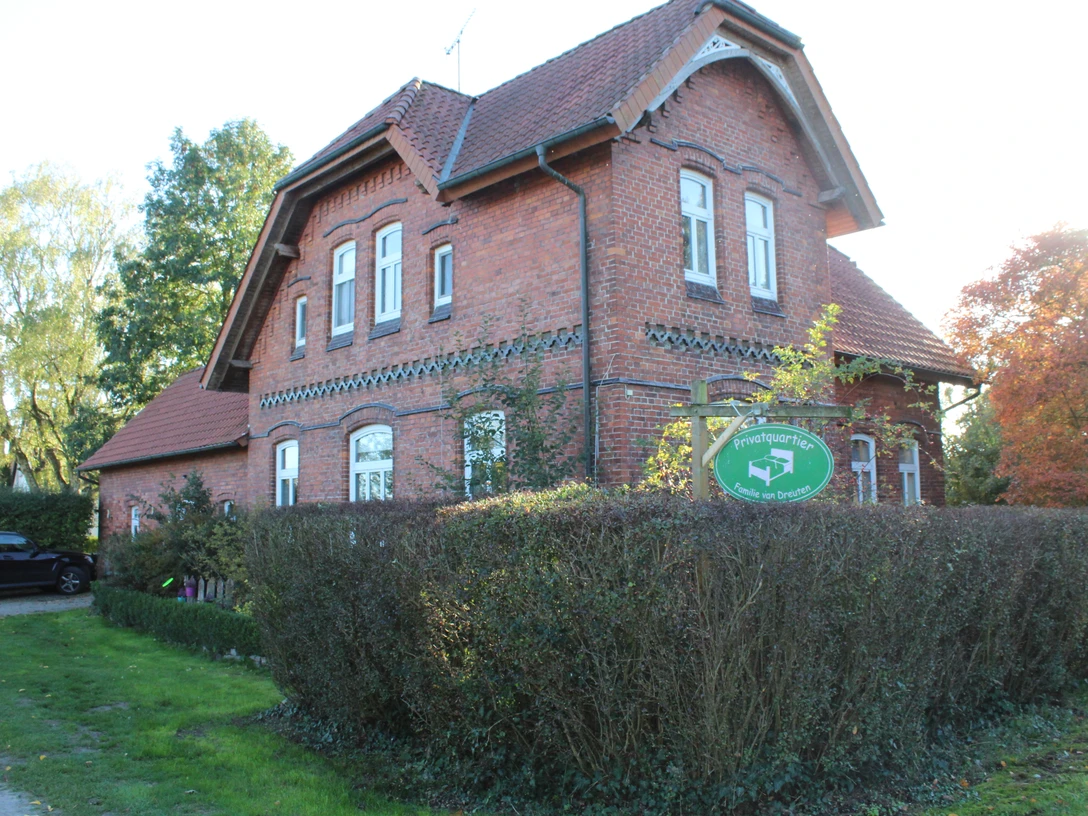van Dreuten Backstein-Haus in ländlicher Umgebung mit gepflegtem Garten und Hecke unter blauem Himmel.