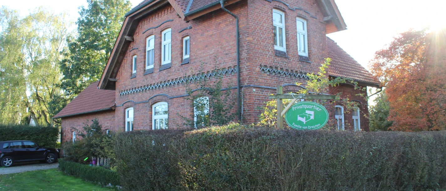 van Dreuten Backstein-Haus in ländlicher Umgebung mit gepflegtem Garten und Hecke unter blauem Himmel.