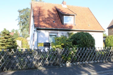 Een vrijstaand huis met een rood pannendak, omringd door bomen, staat achter een houten hek.