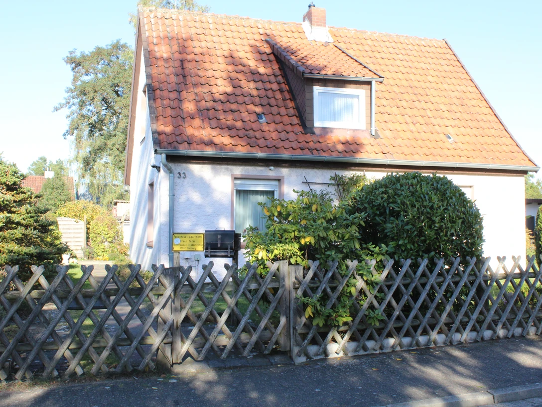 A detached house with a red tiled roof, surrounded by trees, stands behind a wooden fence.