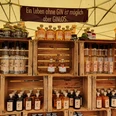 Handwerkermarkt: Gin Marktstand mit Regalen aus Holzkisten, gefüllt mit Gin-, Rum- und Absinthflaschen unter Zeltplane.