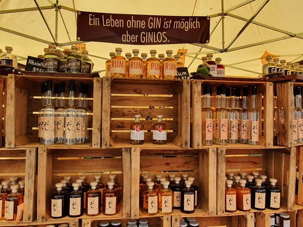 Kunsthandwerkermarkt Greetsiel: Stand mit Gin-Produkten Marktstand mit Regalen aus Holzkisten, gefüllt mit Gin-, Rum- und Absinthflaschen unter Zeltplane.