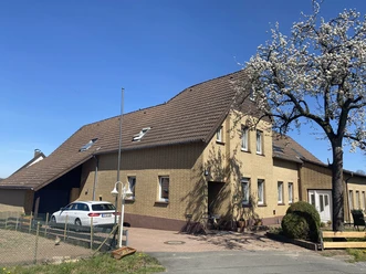 Außenansicht Zweistöckiges gelbes Backsteingebäude mit schrägem Dach, umgeben von blauem Himmel und blühendem Baum.