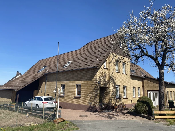 Außenansicht Zweistöckiges gelbes Backsteingebäude mit schrägem Dach, umgeben von blauem Himmel und blühendem Baum.