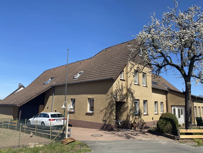 Außenansicht Zweistöckiges gelbes Backsteingebäude mit schrägem Dach, umgeben von blauem Himmel und blühendem Baum.