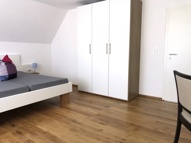 Doppelzimmer Modernes Doppelzimmer mit Holzboden, weißem Schrank und schlichtem Dekor. Funktionale und helle Raumgestaltung.
