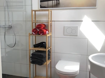 Bad 1 Modernes Badezimmer mit Glasdusche, Holzregal mit Handtüchern, WC und einem Sonnenuntergangsbild.