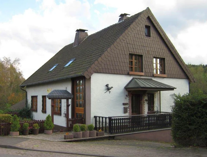 Hausansicht.jpg Ein zweistöckiges, weißes Haus mit dunkelbraunem Walmdach und weißen Holzfenstern in ruhiger Lage.