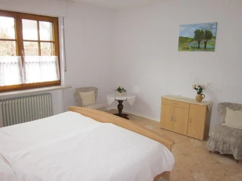 Schlafzimmer Helles Schlafzimmer mit Doppelbett, zwei Sesseln, hellem Holzschrank und Fenster mit weißem Vorhang.