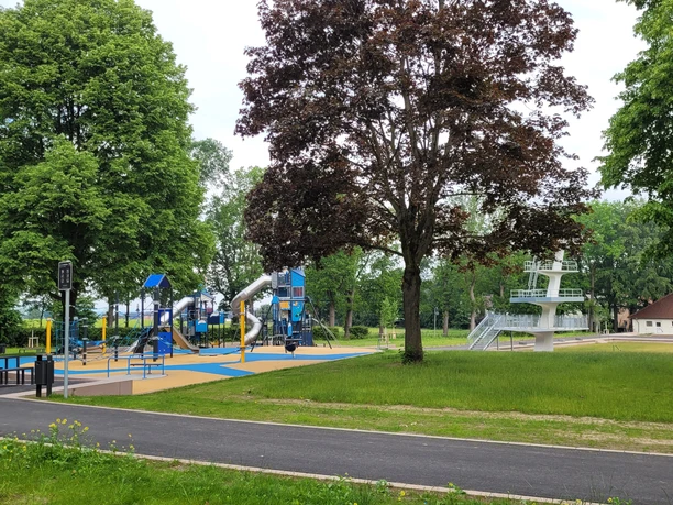 Freibadpark Lübbecke Freizeitpark mit Spielanlage, Wasserrutsche und Sprungturm, umgeben von grüner Natur und Bäumen.