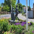 Danzelstätte Lübbecke Bronzeskulptur eines tanzenden Paars inmitten eines bunt blühenden Blumenbeets vor Fachwerkhäusern.