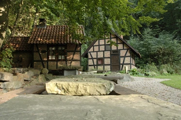 Kummerbrink Andreas Sieveking Fachwerkhäuser im Grünen, umgeben von Bäumen und Pflasterweg, strahlen Ruhe und Naturverbundenheit aus.