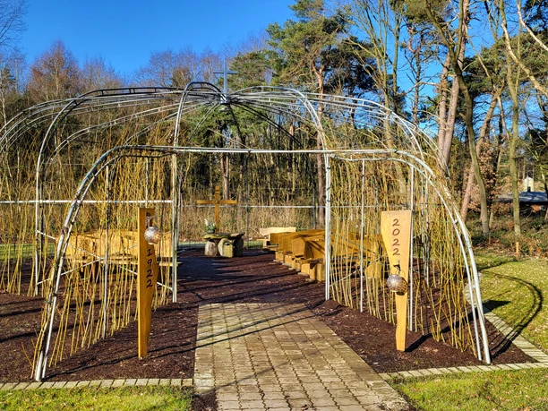 Weidenkirche in Lahn (3) © Naturpark Hümmling e. V..jpg Offene Weidenkirche mit Holzbänken und Kreuz inmitten einer grünen Waldlichtung unter blauem Himmel.