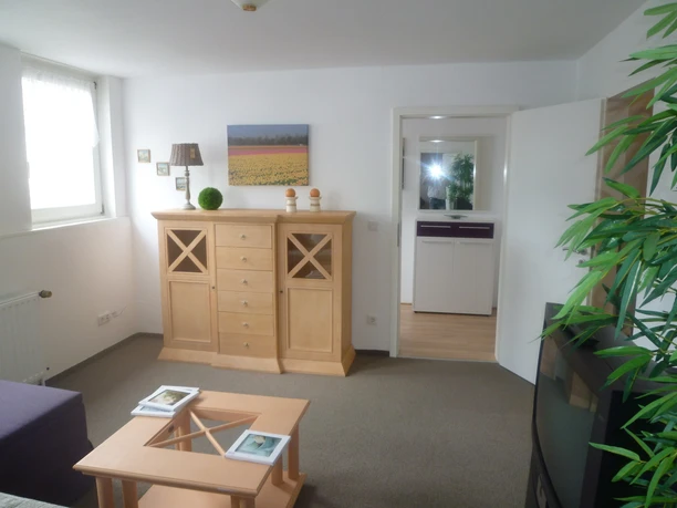 Fewo Höcker_Wohnzimmer1 Bild3.JPG <p>Wohnzimmer mit Holzschrank, Couch, Couchtisch und heller Tür zu Flur, wohnlich und einladend.</p>