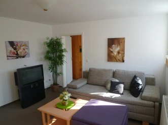 053_Fewo Höcker_Wohnzimmer.JPG <p>Gemütliches Wohnzimmer in neutralen Tönen mit grauem Sofa und dekorativen Blumenbildern.</p>