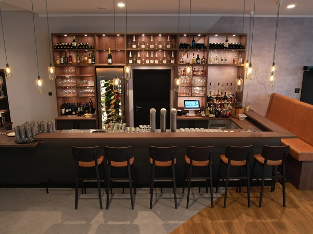 Bar.JPG Moderne Hotelbar mit Holztheke, stilvoller Beleuchtung und Sitzplätzen vor gut sortiertem Regal.