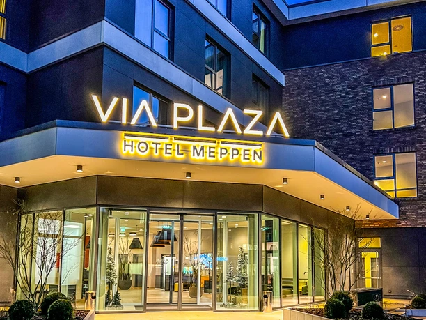VIA PLAZA.jpeg Eingangsbereich des VIA PLAZA Hotel Meppen mit leuchtendem Schriftzug bei Abendbeleuchtung.