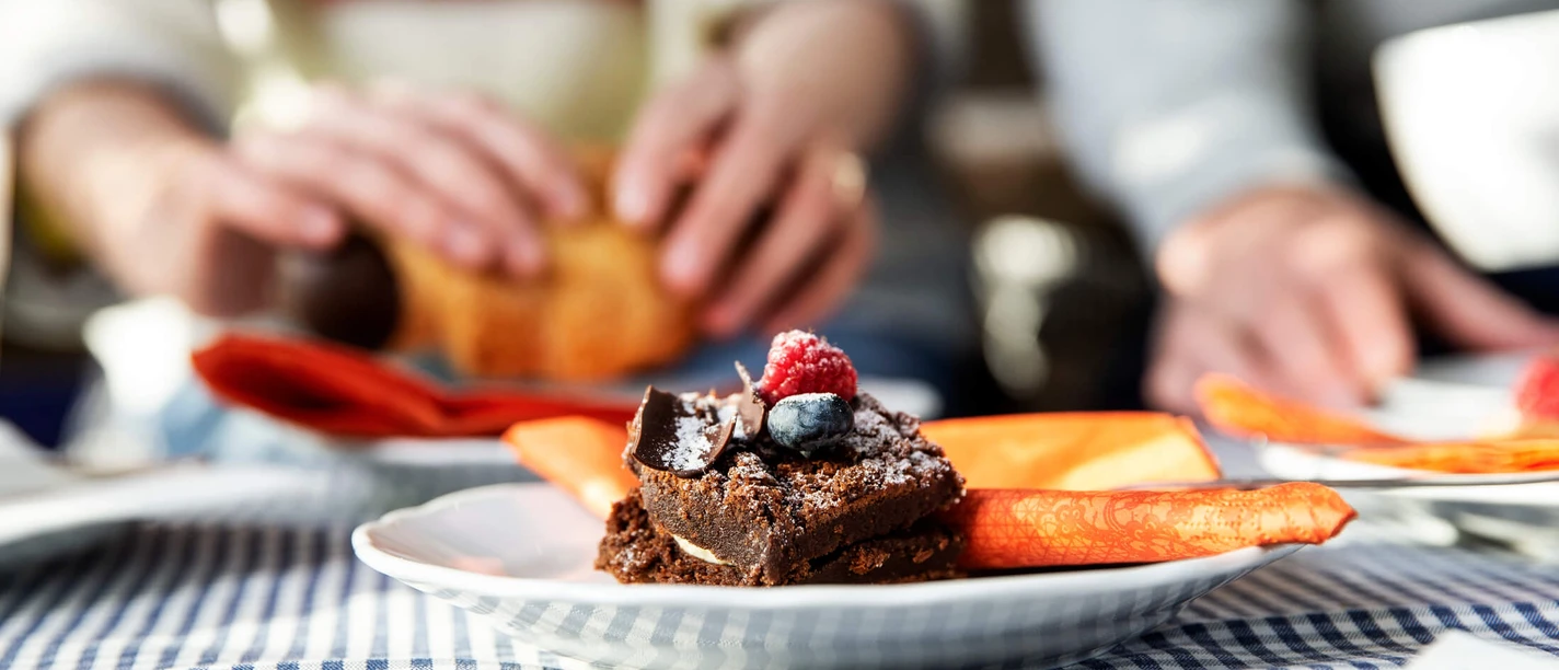 Een bord chocoladetaart gegarneerd met frambozen en bosbessen op een geruit tafelkleed.