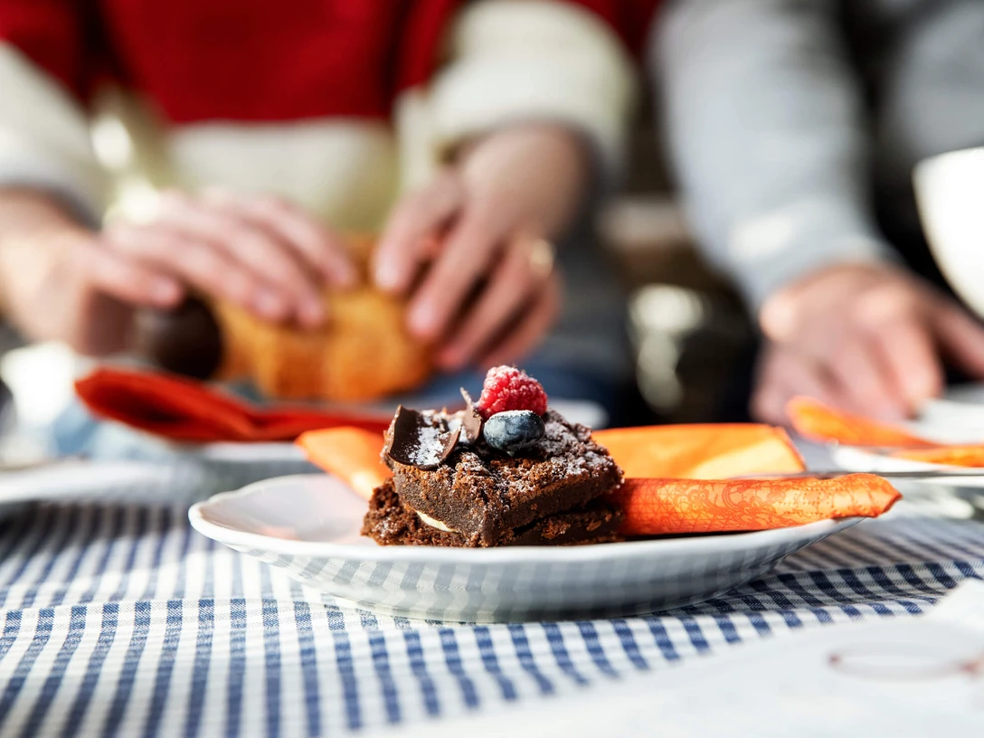 Café Symbolbild Ein Teller mit Schokoladenkuchen, garniert mit Himbeeren und Blaubeeren auf kariertem Tischtuch.