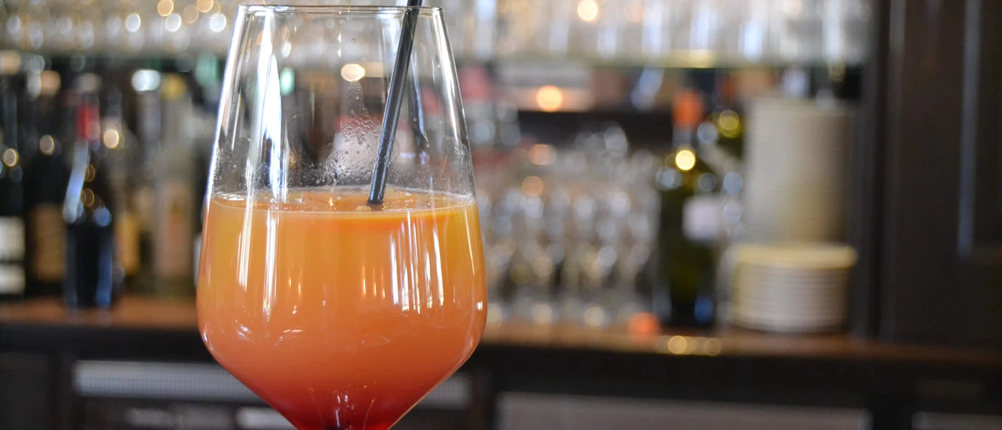 Een cocktailglas met een oranje drankje, rode basis en rietje voor een wazige achtergrond van een bar.