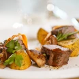 Fein angerichtete Speisen mit Kartoffeln, saftigem Fleisch und Kräutern auf einem weißen Teller.