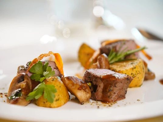 Fein angerichtete Speisen mit Kartoffeln, saftigem Fleisch und Kräutern auf einem weißen Teller.