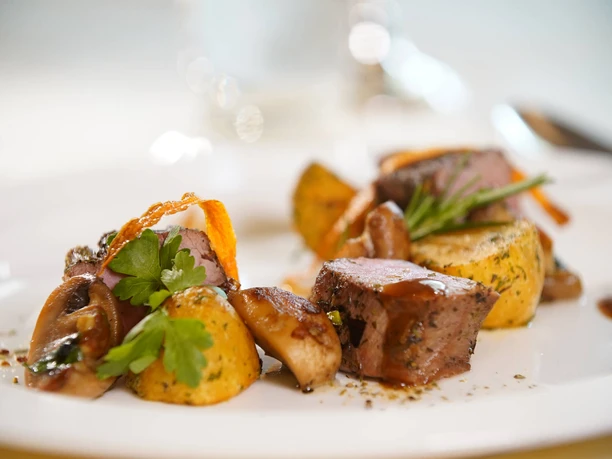 Restaurant Symbolbild Fein angerichtete Speisen mit Kartoffeln, saftigem Fleisch und Kräutern auf einem weißen Teller.