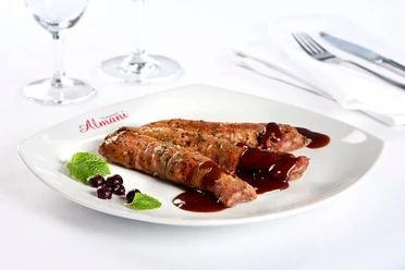Genuss im Almani Zwei saftige Fleischröllchen mit roter Sauce und Kräutern auf einem Teller mit Almani-Logo.