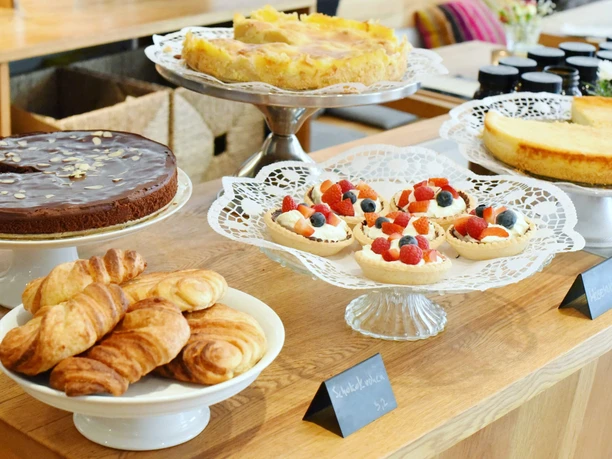 Various cakes and croissants on a wooden counter, presented on decorative cake stands in the café.
