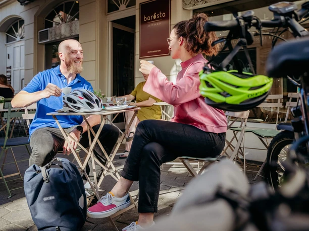 Two people enjoy drinks in the sunshine at an outdoor table at Café Barösta in Osnabrück.