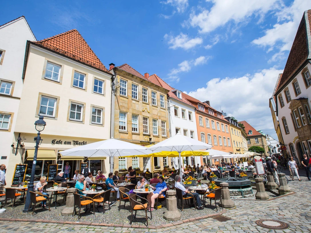 Menschen genießen sonnige Stunden vor einem historischen Café in einer belebten Altstadtkulisse.