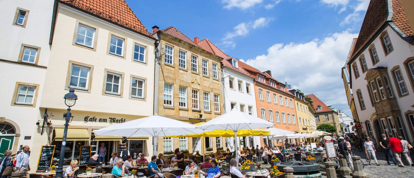 People enjoy sunny hours in front of a historic café in a lively old town setting.