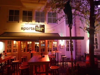 Joe Enochs Sportsbar Sportsbar in Abendstimmung, beleuchtet mit Neonlicht, umgeben von Bäumen mit blühendem Blätterwerk.