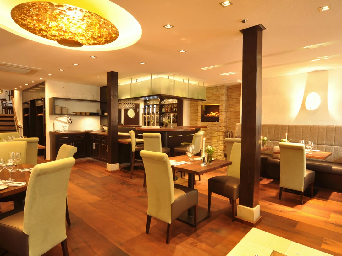 Elegantes Restaurantinterior mit Holztischen, gepolsterten Stühlen und moderner Beleuchtung.