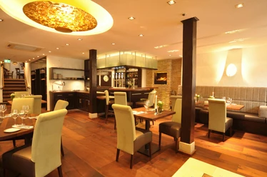Romantik Restaurant Walhalla Elegantes Restaurantinterior mit Holztischen, gepolsterten Stühlen und moderner Beleuchtung.