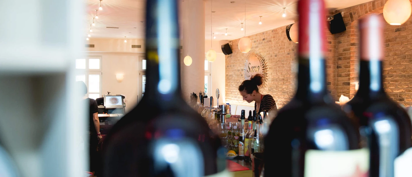 Interior view of a restaurant with a brick wall, in front of which a woman is working next to a bottle of drink.