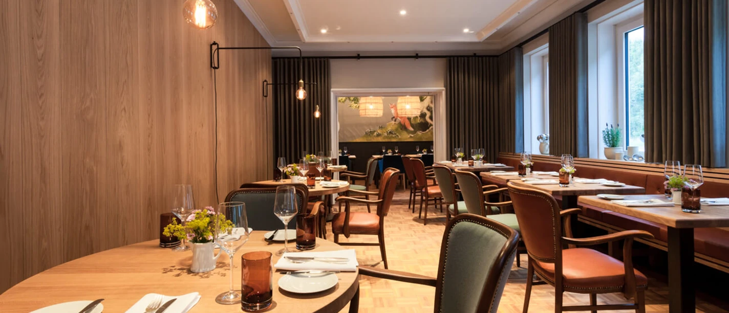 Vox Drink & Dine im Haus Rahenkamp Ein elegantes Restaurant mit modernen Holzmöbeln, gedeckten Tischen und großen Fenstern.