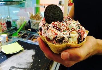 Eisdiele Schlecks in Osnabrück Ein Waffelbecher voller Eis mit bunten Streuseln und Oreo dekoriert, in einer Hand gehalten.
